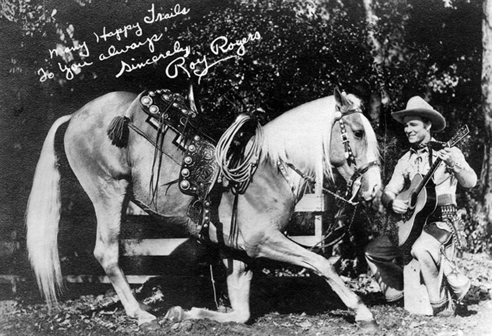 Trigger kneeling next to Roy Rogers who is playing a guitar