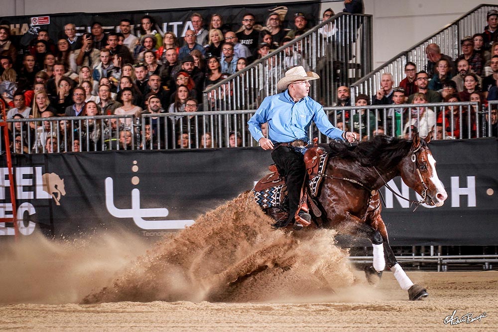 Cowboy in blue shirt with hat on a horse doing a sliding stop